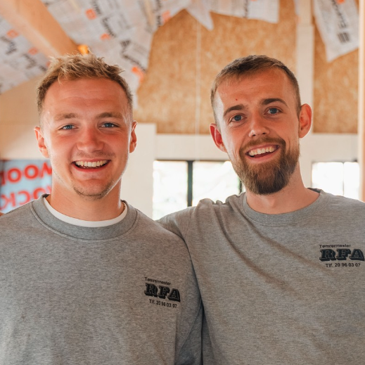 Nærbillede af to smilende mænd i RFA-sweatshirts med armene om hinanden indendørs.